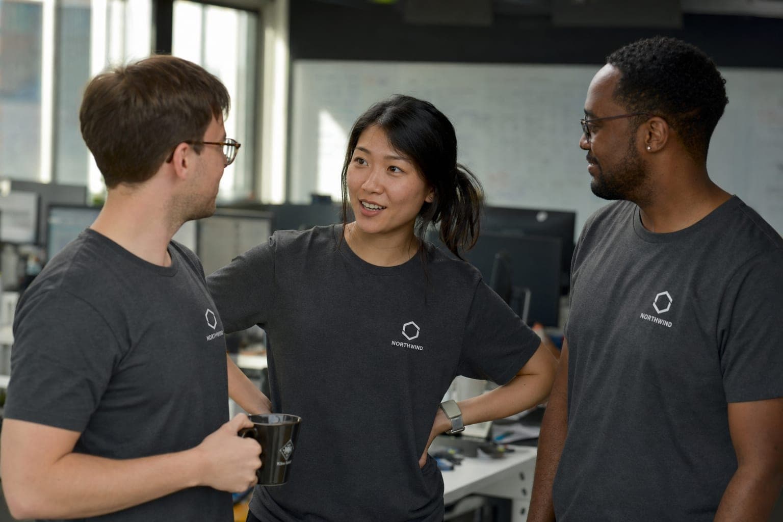 Three colleagues in an office wearing matching charcoal team shirts